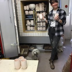 Apprentice Sarah Wilson in front of the kiln holding two mugs